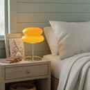 Yellow table lamp on a nightstand next to a bed with pillows and books.