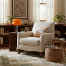 Beige armchair in a living room with a patterned rug, wicker basket, and decorative items.