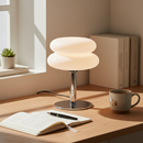 Modern table lamp on a desk with a cup, pen, and open book in a bright room.