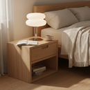 Wooden nightstand with lamp, book, and mug next to a bed in a bedroom.