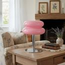 Pink modern stool on a wooden table in a living room setting with a floral-patterned sofa and framed pictures on the wall.