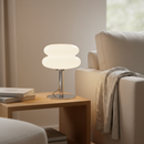 Modern table lamp on a wooden side table next to a beige armchair with a blanket.