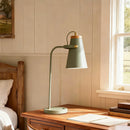 Green desk lamp on a wooden desk with a window in the background