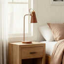 Wooden nightstand with a brown lamp next to a bed with white and beige bedding.