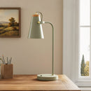 Green desk lamp on a wooden desk with a painting in the background