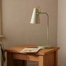 Green desk lamp on a wooden table with a magazine against a beige wall