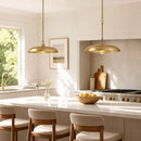 Two brass pendant lights hang over a white kitchen island with cream upholstered bar stools in a bright, modern kitchen.