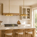 A bright, modern kitchen with two hanging brass pendant lights over a marble island, white subway tile backsplash, wood cabinetry, and three woven-back bar stools.