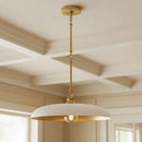 Ceiling light fixture with white shade and gold trim in a room with wooden ceiling and windows.