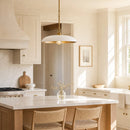 A modern kitchen island with a white marble countertop and light wood base, featuring two woven bar stools. A white dome pendant light with a gold-toned frame hangs above.