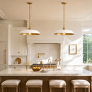 Two modern pendant lights with white dome-shaped shades and brushed gold hardware hang over a white marble kitchen island in a bright, elegant kitchen with white cabinets and gold fixtures.