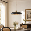 A black and brass pendant light hanging over a dining table in a bright, elegant room with cream walls, woven-back chairs, and floral arrangements.