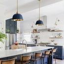 Modern kitchen with blue pendant lights, white countertops, and wooden chairs.