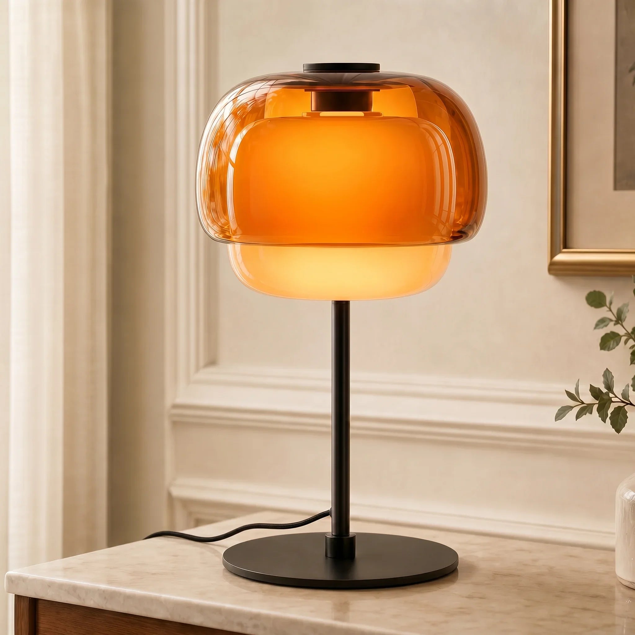 Table lamp with orange glass shade on a marble surface, with a neutral wall and plant in the background.