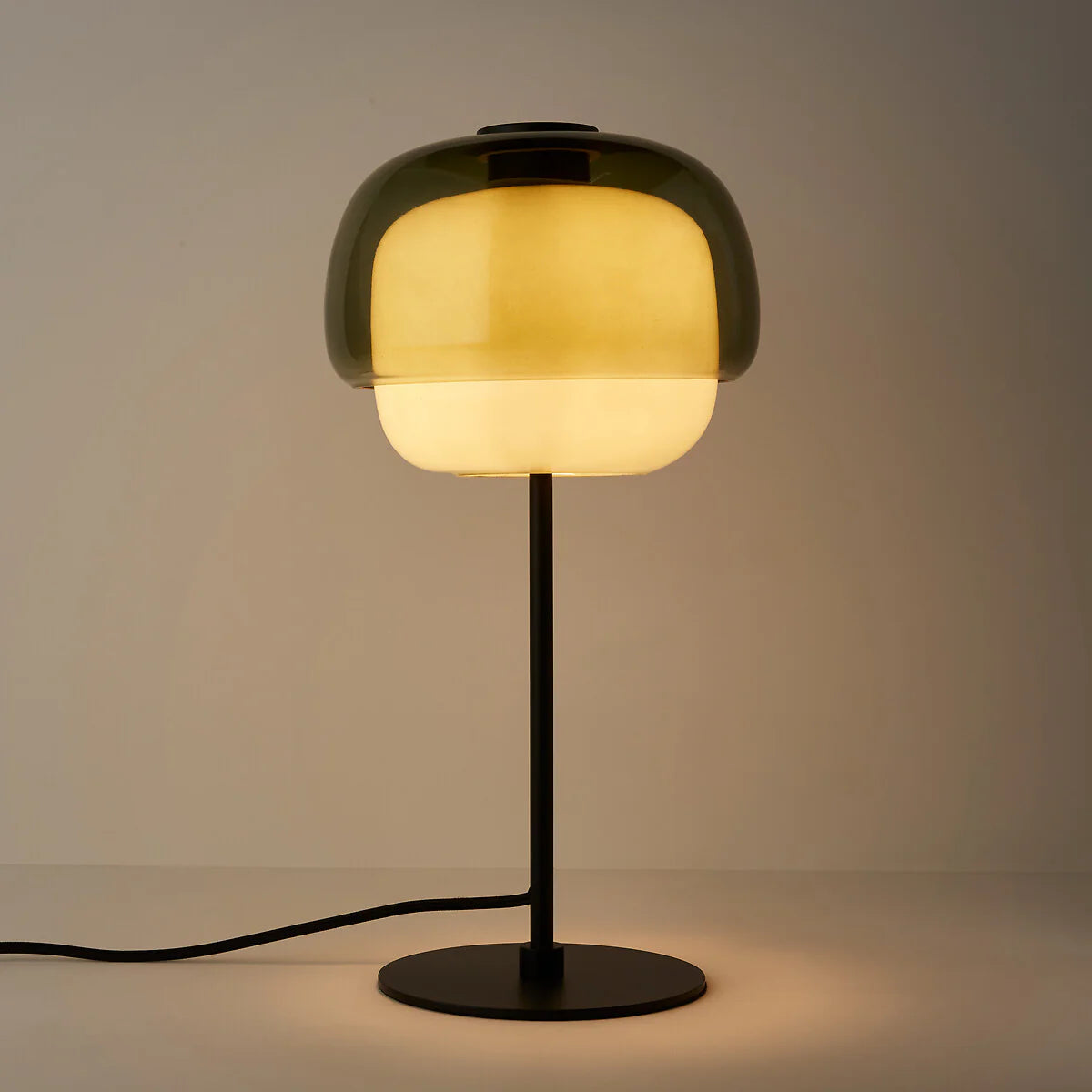 Table lamp with a glass shade emitting a warm glow on a neutral background