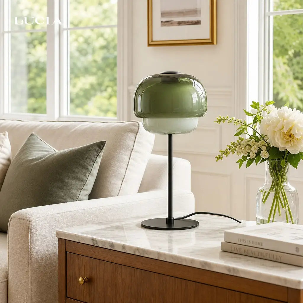 Green glass table lamp on a marble surface with a couch and window in the background