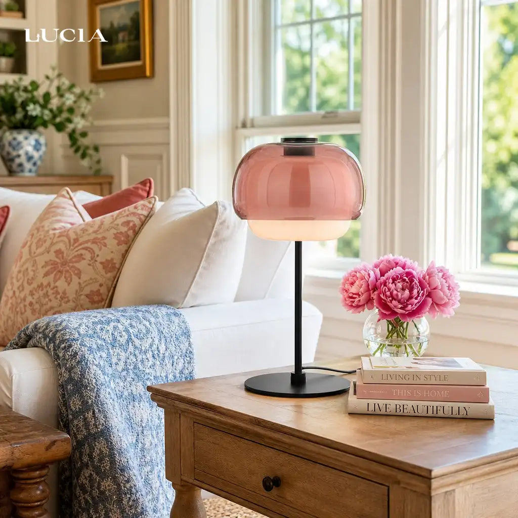 Pink lamp on a wooden table with books and flowers in a living room setting.