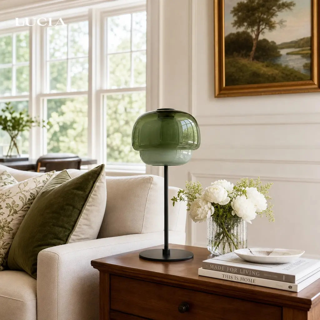 Green table lamp on a wooden coffee table in a living room with a couch and decorative items.