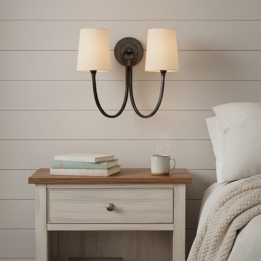 Wooden nightstand with books and a mug next to a bed with a wall sconce above.