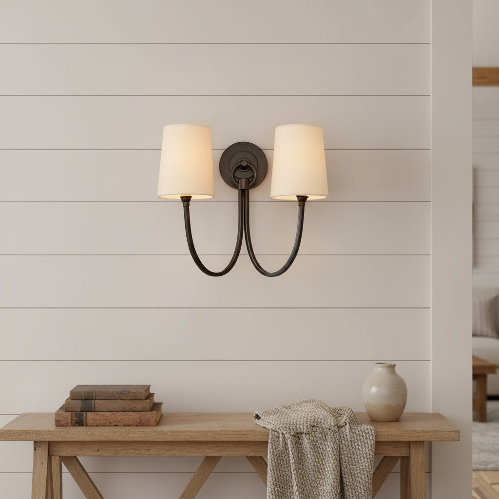 Wall-mounted double-sconce light fixture on a wooden wall with a wooden bench and decor items below.