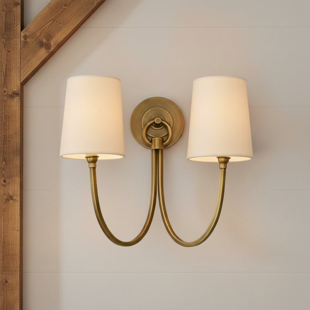 Double wall sconce with brass fixture and white lampshades on a neutral wall.