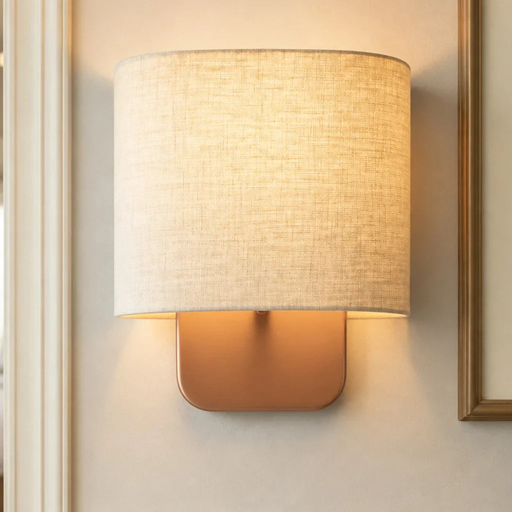 Wall-mounted lamp with a textured beige shade and gold base on a neutral wall.