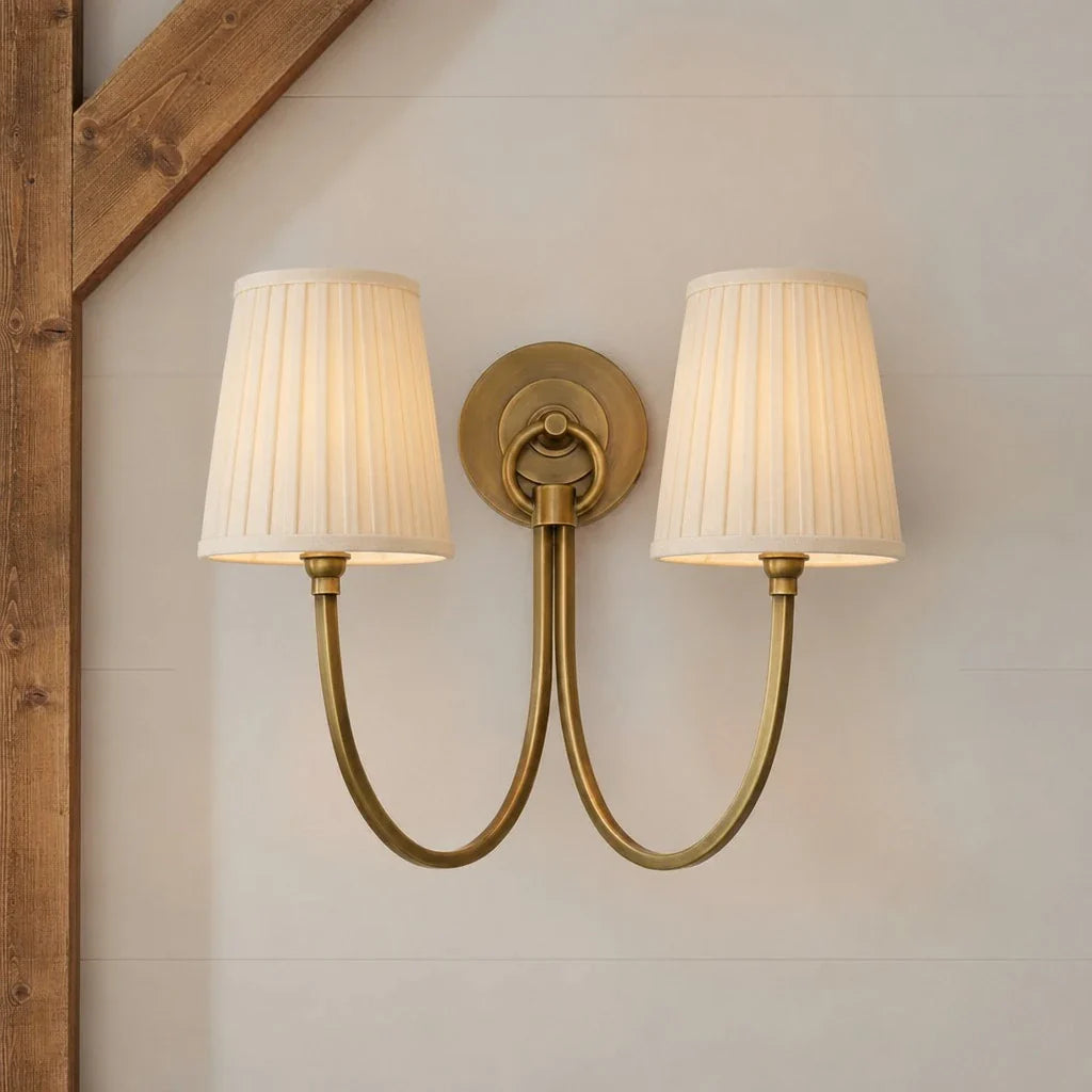 Double wall sconce with pleated lampshades on a neutral wall.