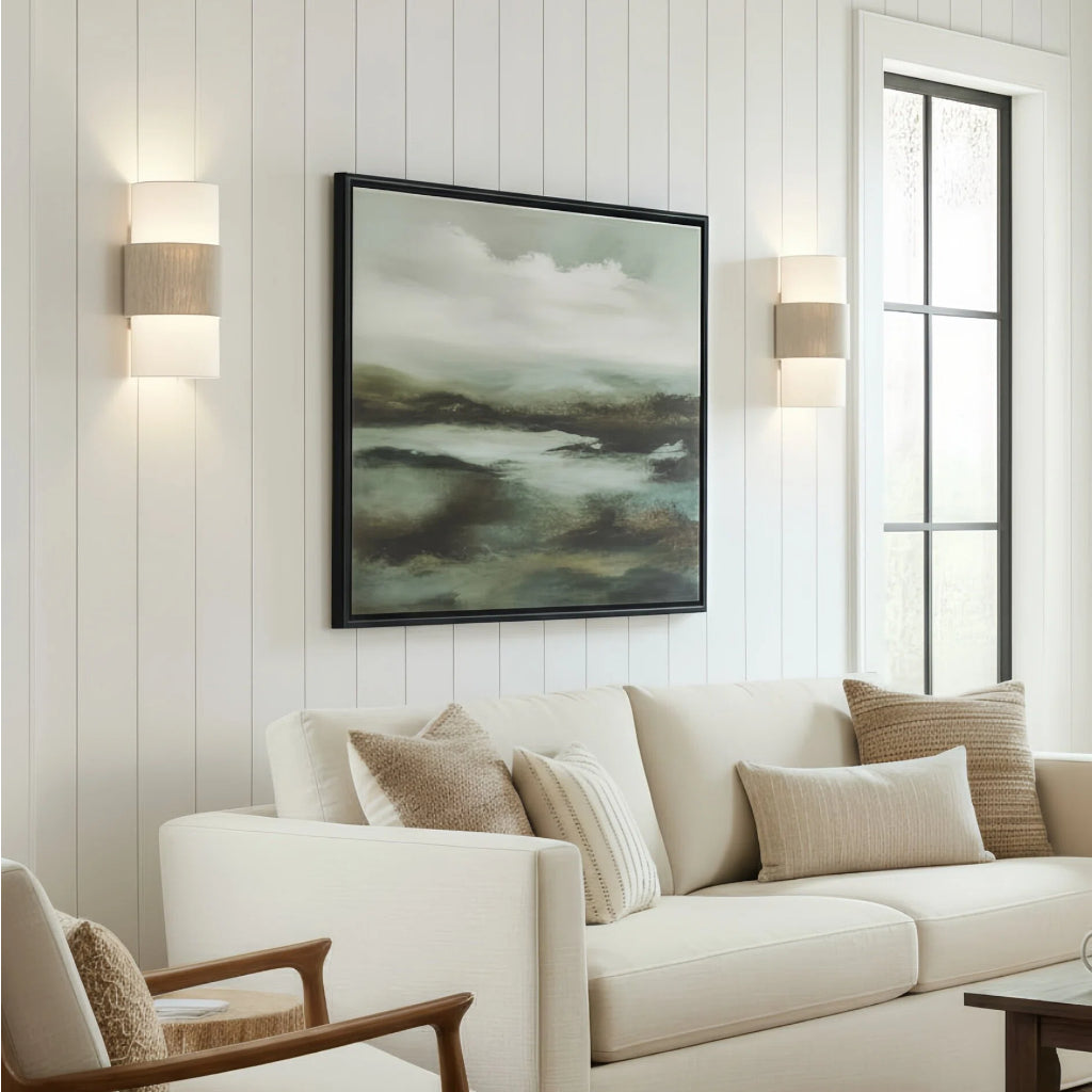 Living room with a white sofa, decorative pillows, and a framed landscape painting on the wall.