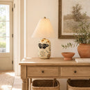 Decorative lamp with butterfly design on a wooden table in a room with a painting and plants.