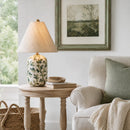 Living room with a lamp on a side table, a sofa with a blanket and pillow, and a framed picture on the wall.