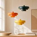 Three colorful pendant lights hanging in a room with a window and books on a surface.