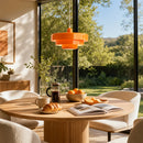 Round wooden table with coffee, croissant, and oranges in a room with large windows showing a garden view.