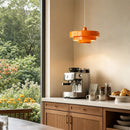 Modern kitchen with espresso machine, orange pendant light, and view of greenery outside.