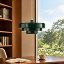 Green pendant light hanging above a desk with an open book and a cup, with a window showing a view of trees and sky.