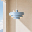 Blue pendant light hanging against a beige wall with sunlight casting shadows.
