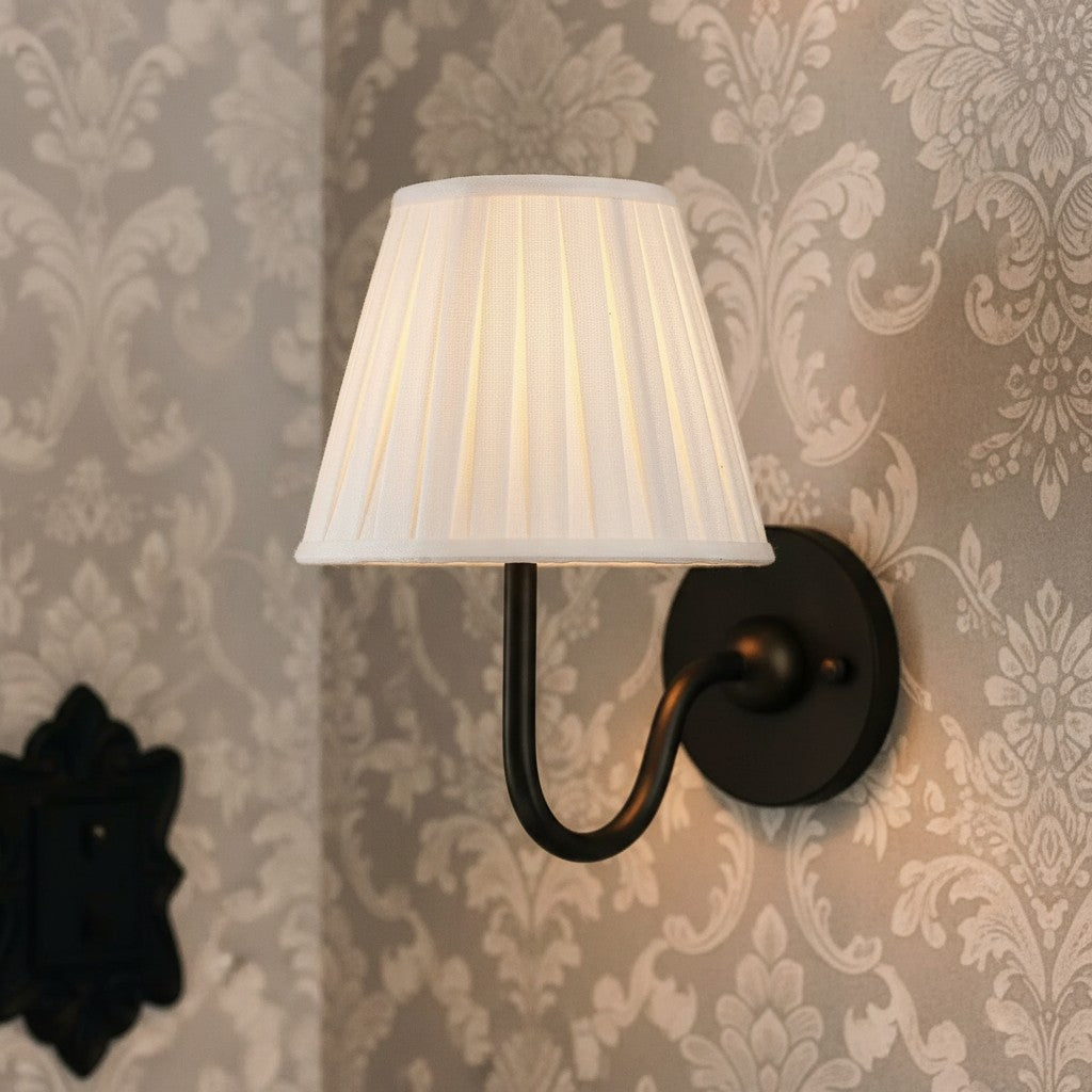 Wall-mounted lamp with pleated white shade against decorative wallpaper