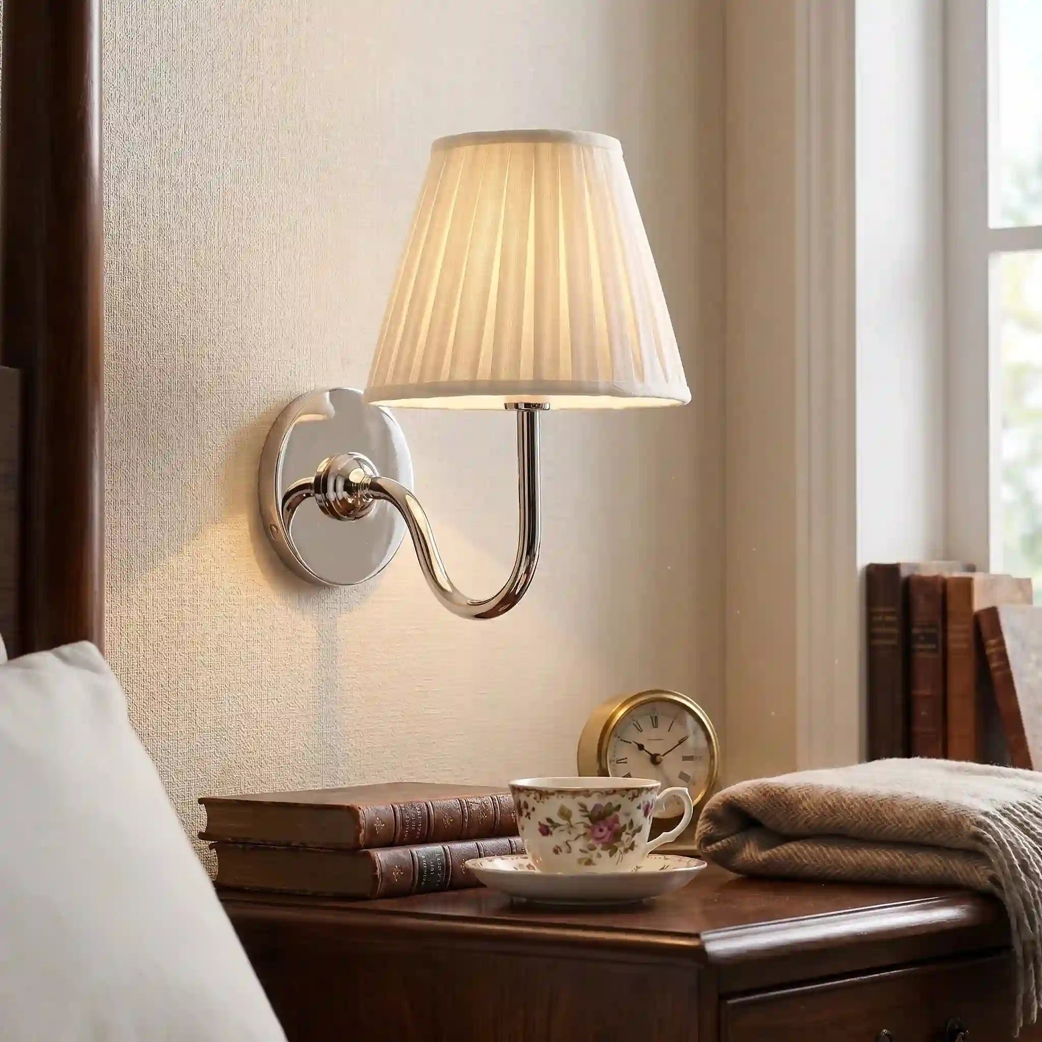 Wall-mounted lamp on a nightstand with books, a cup, and a clock in a bedroom setting.
