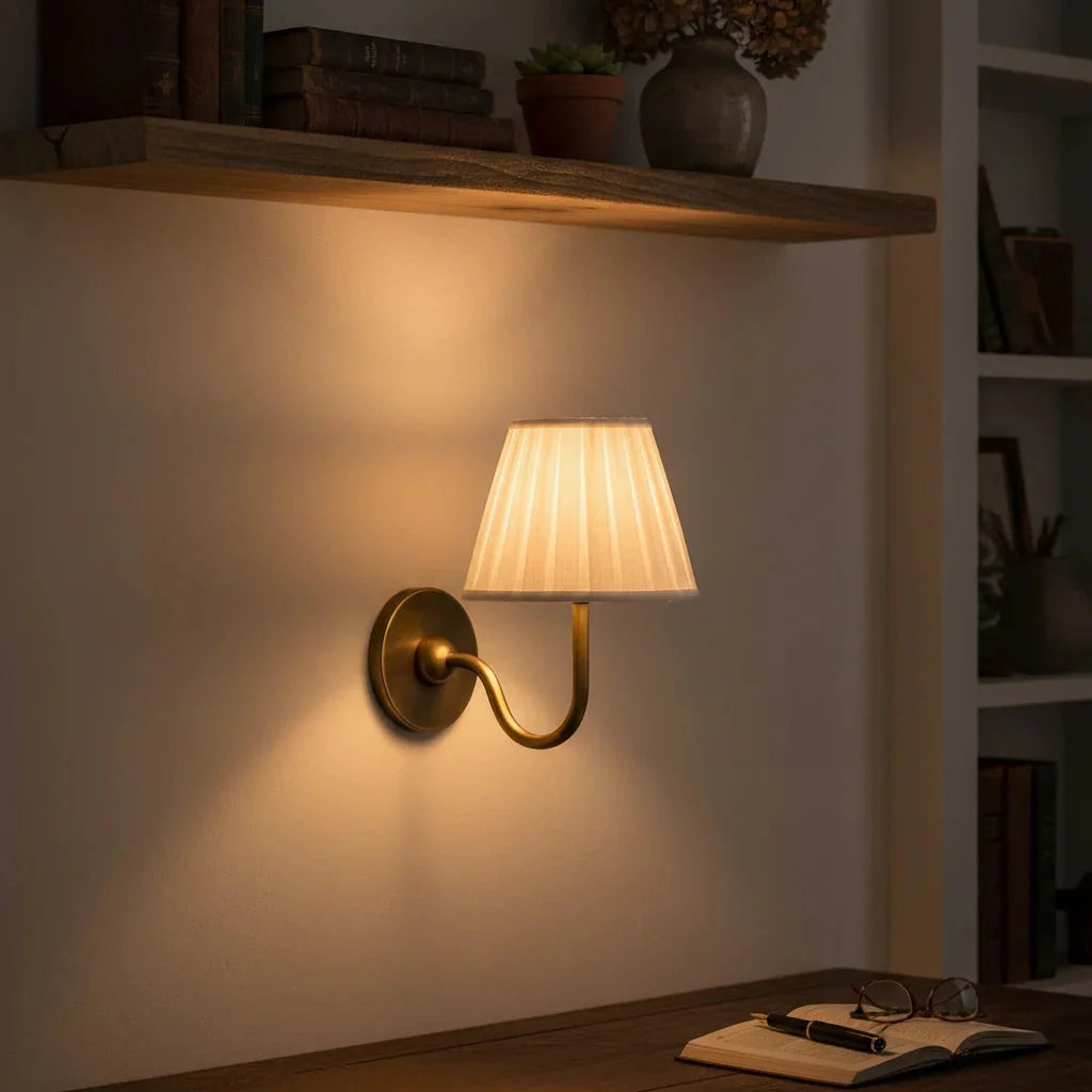 Wall-mounted lamp with pleated shade on a wall in a cozy room setting.