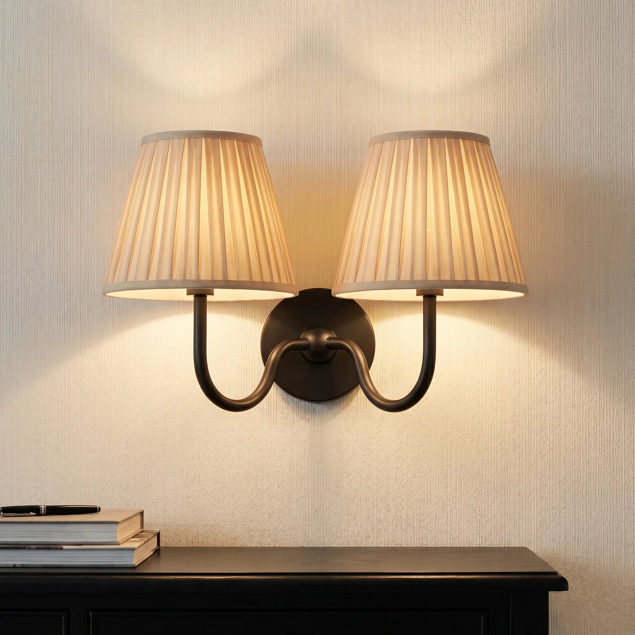 Wall-mounted lamp with two beige shades on a textured wall.