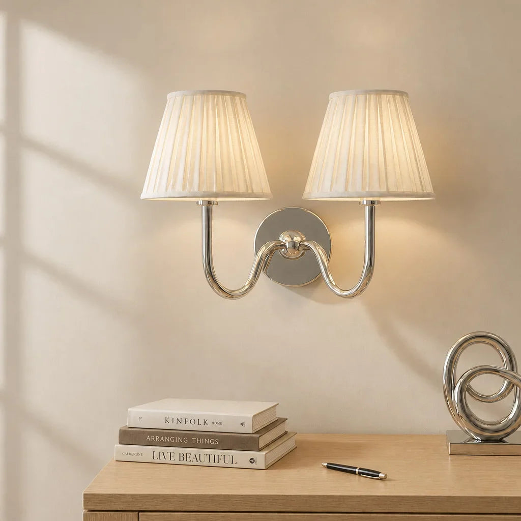 Wall sconce with pleated lampshades above a wooden surface with books and decor items.