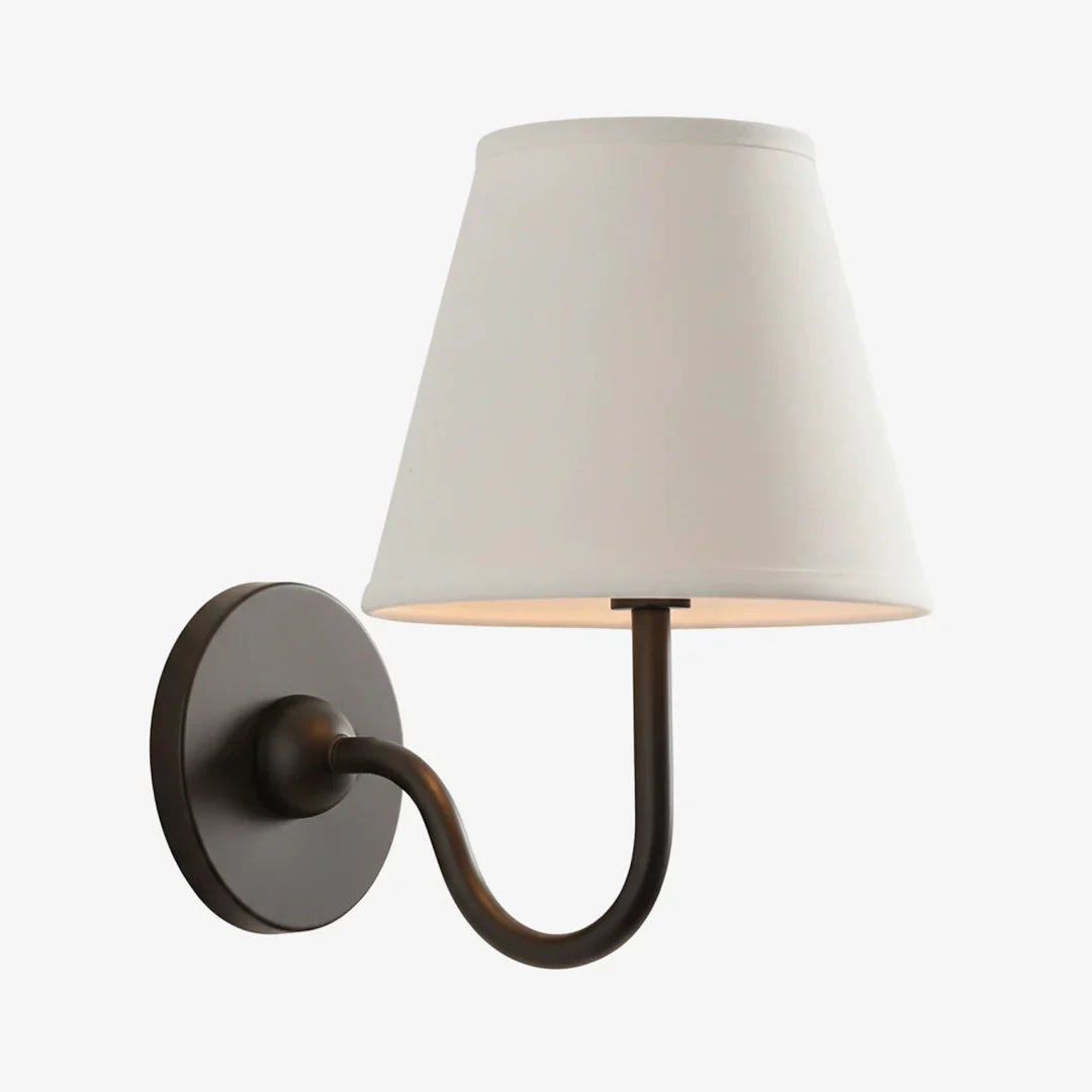A modern wall sconce light fixture with a tapered off-white fabric shade, a curved dark metal arm, and a round wall plate, shown against a plain light gray background.