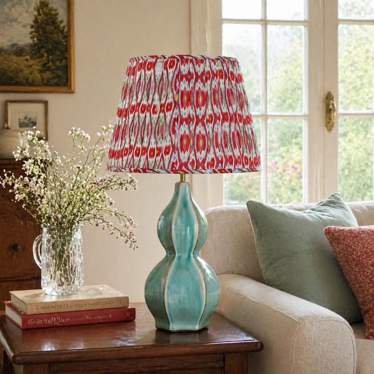 A table lamp with a turquoise-green sculptural base and a red-and-white patterned drum shade, placed on a wooden side table in a living room setting.