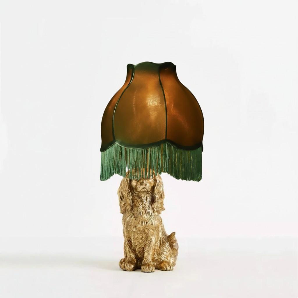 Decorative lamp with a dog-shaped base and green fringed shade on a white background