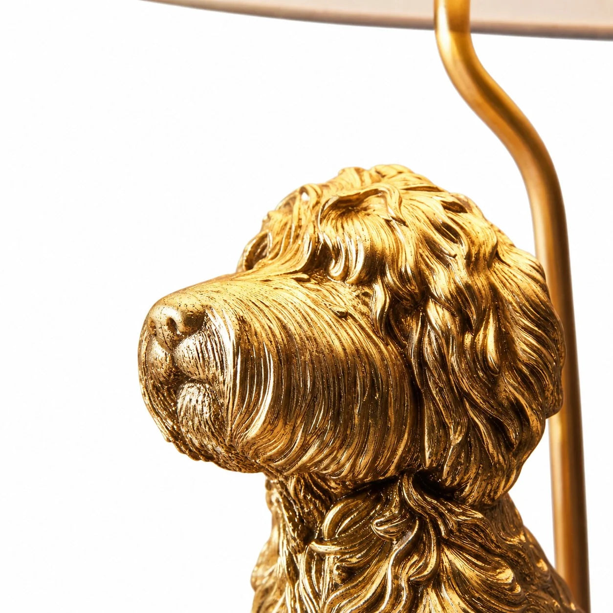 Close-up of a metallic gold dog-shaped decorative object or lamp base on a white background, with part of a curved gold support arm visible at the top right.