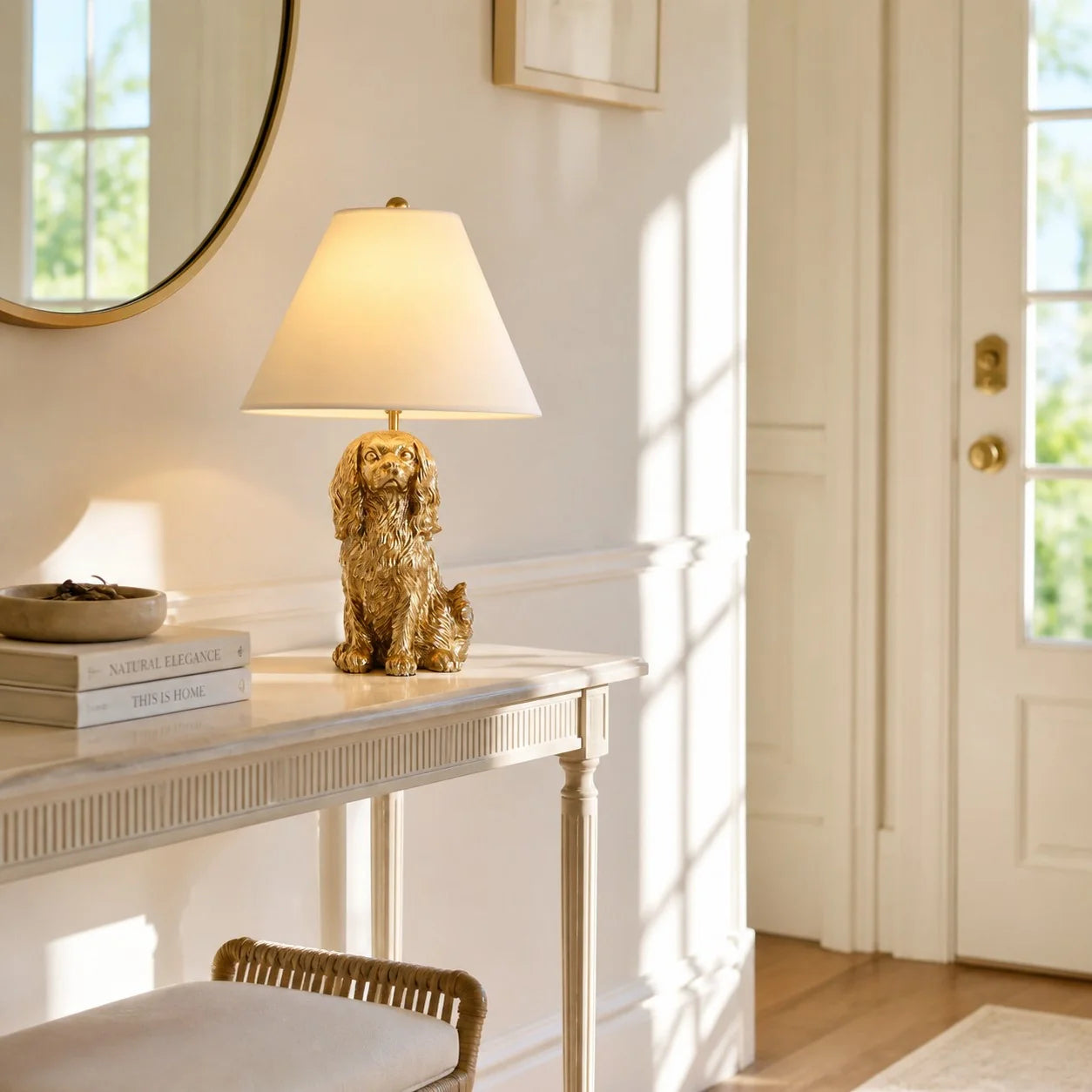 A gold-colored dog figurine table lamp with a cream-colored conical shade, styled on a white console table in a bright, sunlit room.
