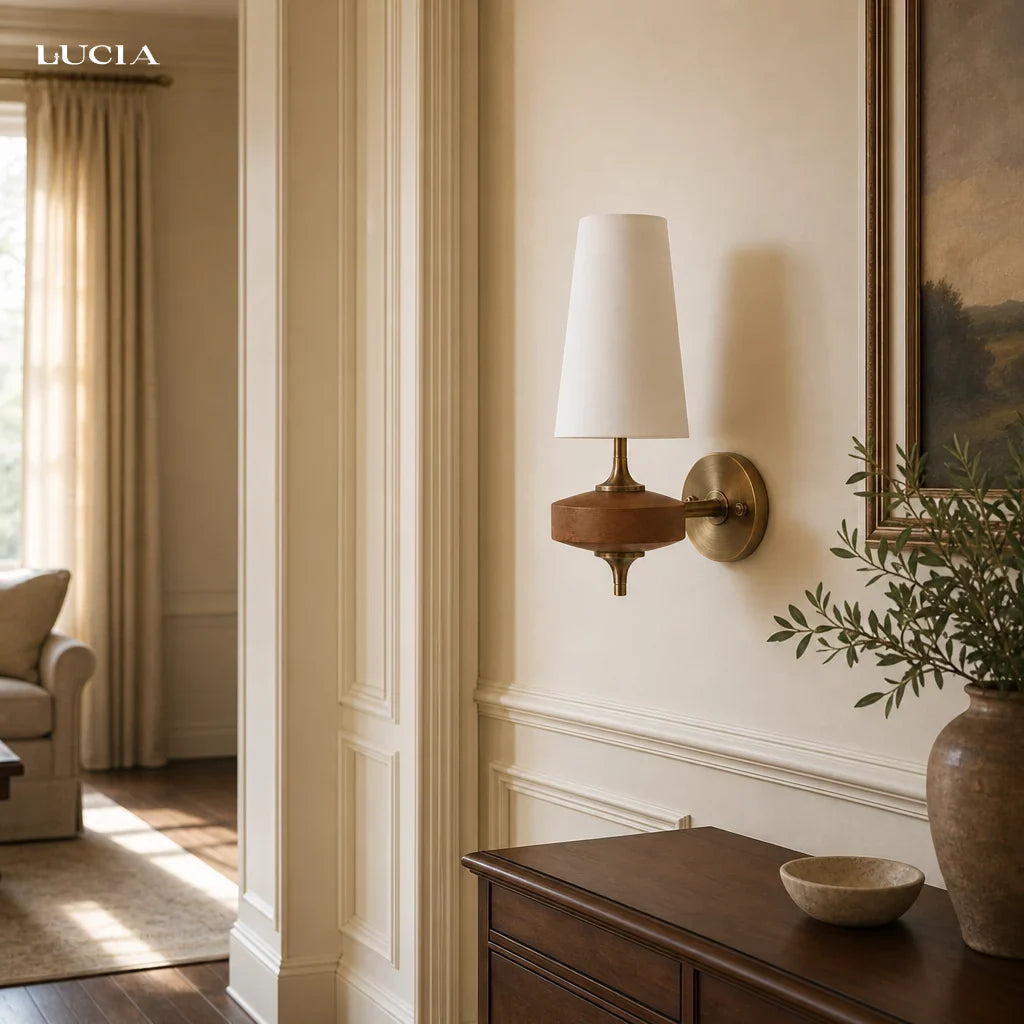 Wall sconce with a white lampshade in a room with a painting and plant.
